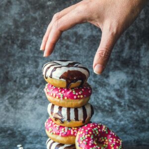 A hand reaches for a stack of colorful donuts with chocolate drizzle and sprinkles, tempting and delicious.